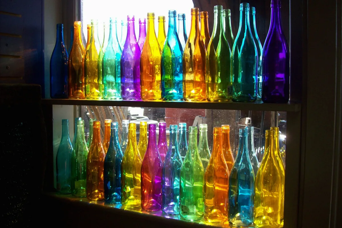 Des flacons de verre colorés sur des étagères devant une fenêtre lumineuse