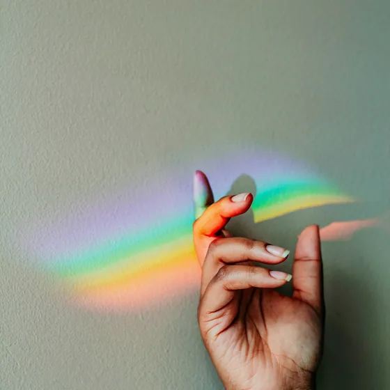 Une main devant un reflet d'arc-en-ciel sur un mur vert-gris
