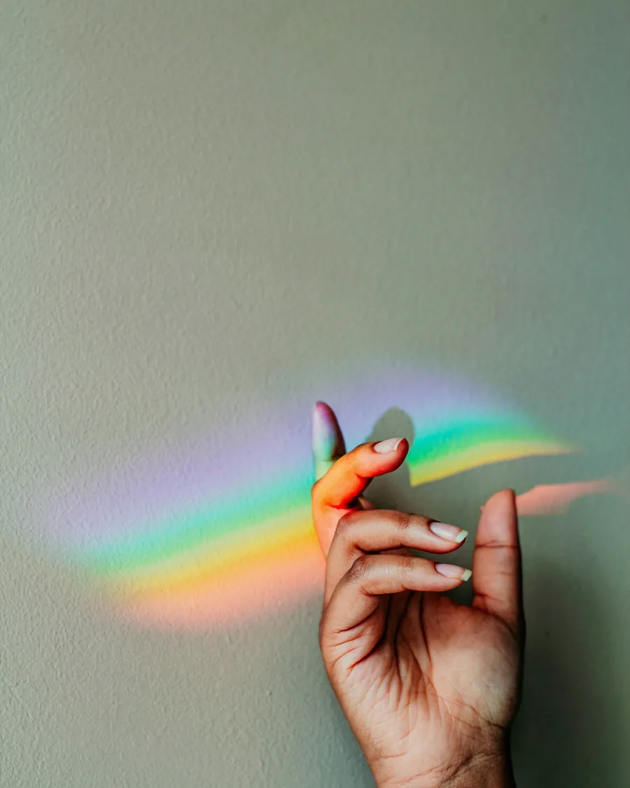 Une main devant un reflet d'arc-en-ciel sur un mur vert-gris