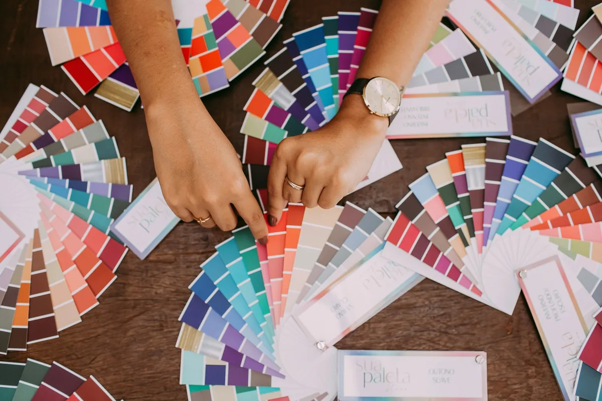 Deux mains manipulent des nuanciers de couleurs étalés sur une table en bois